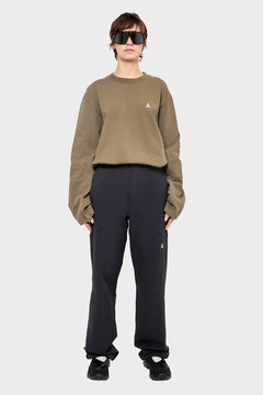 Modelka w dużych okularach, luźna beżowa bluza, czarne spodnie, styl streetwear