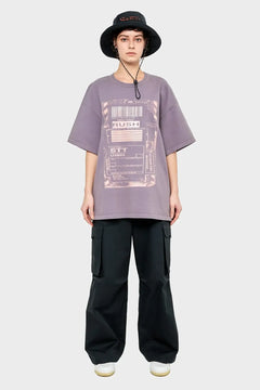 Osoba w luźnym fioletowym t-shircie z nadrukiem, czarnych bojówkach i czarnym kapeluszu typu bucket hat
