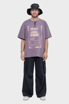 Mężczyzna w fioletowym t-shircie z nadrukiem, czarnych bojówkach i bucket hat, styl streetwear