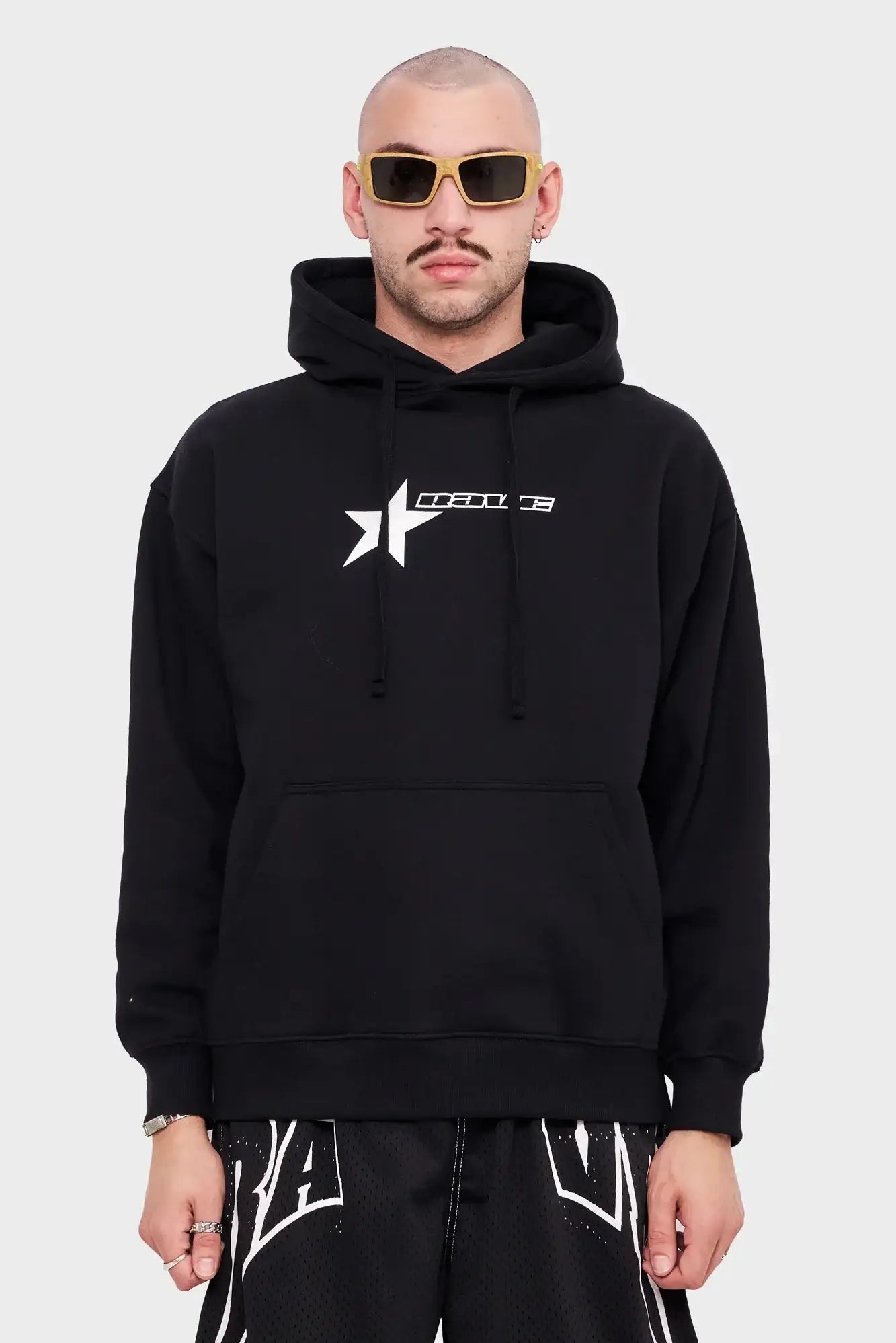 Mężczyzna w czarnej bluzie z kapturem i białym logo, żółte okulary, styl streetwear