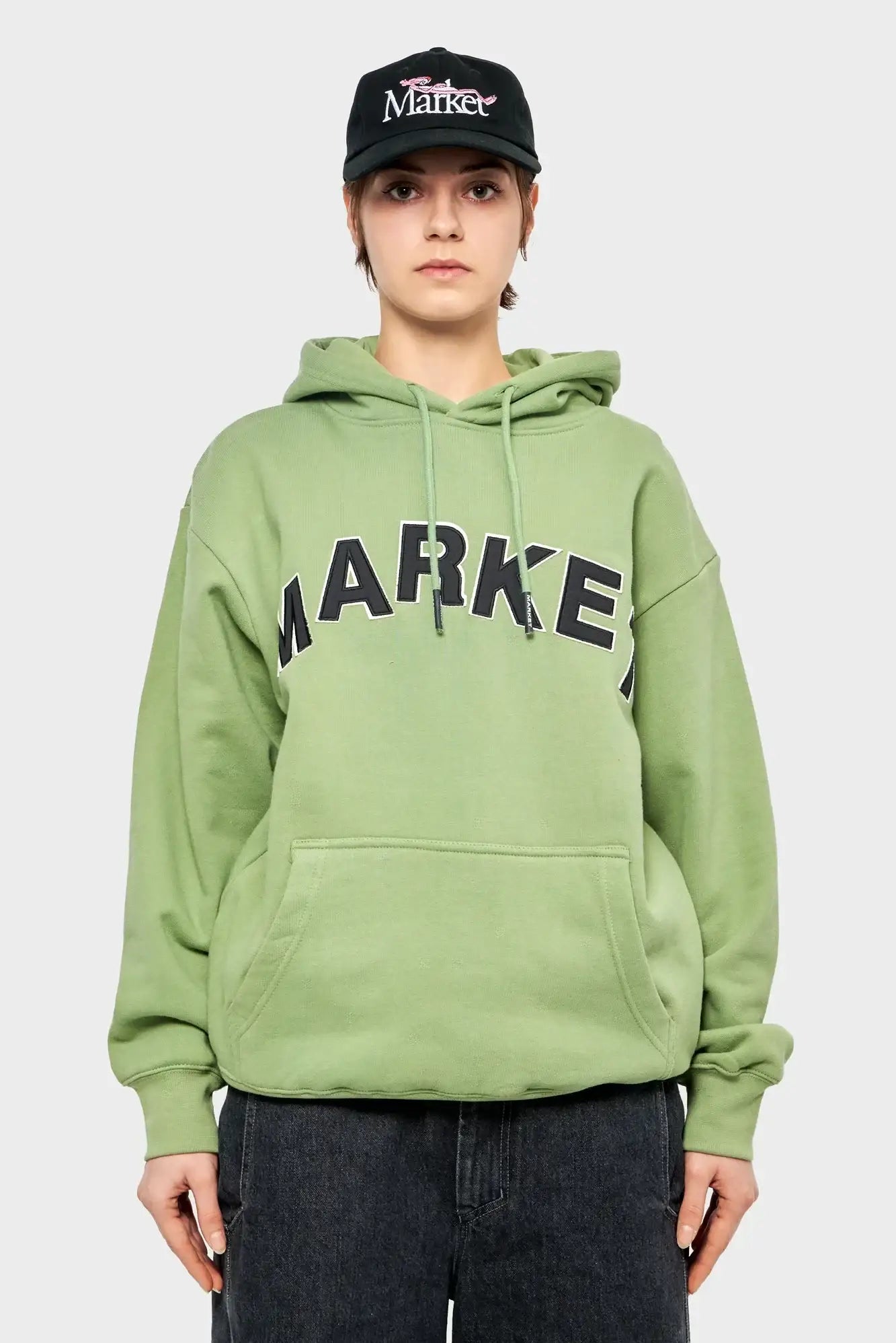 Modelka w zielonej bluzie z kapturem Market, czarna czapka z daszkiem, styl streetwear
