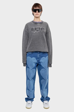 Osoba w szarych okularach, bluzie z napisem i dżinsach z niebieskimi sercami, nowoczesna stylizacja streetwear.