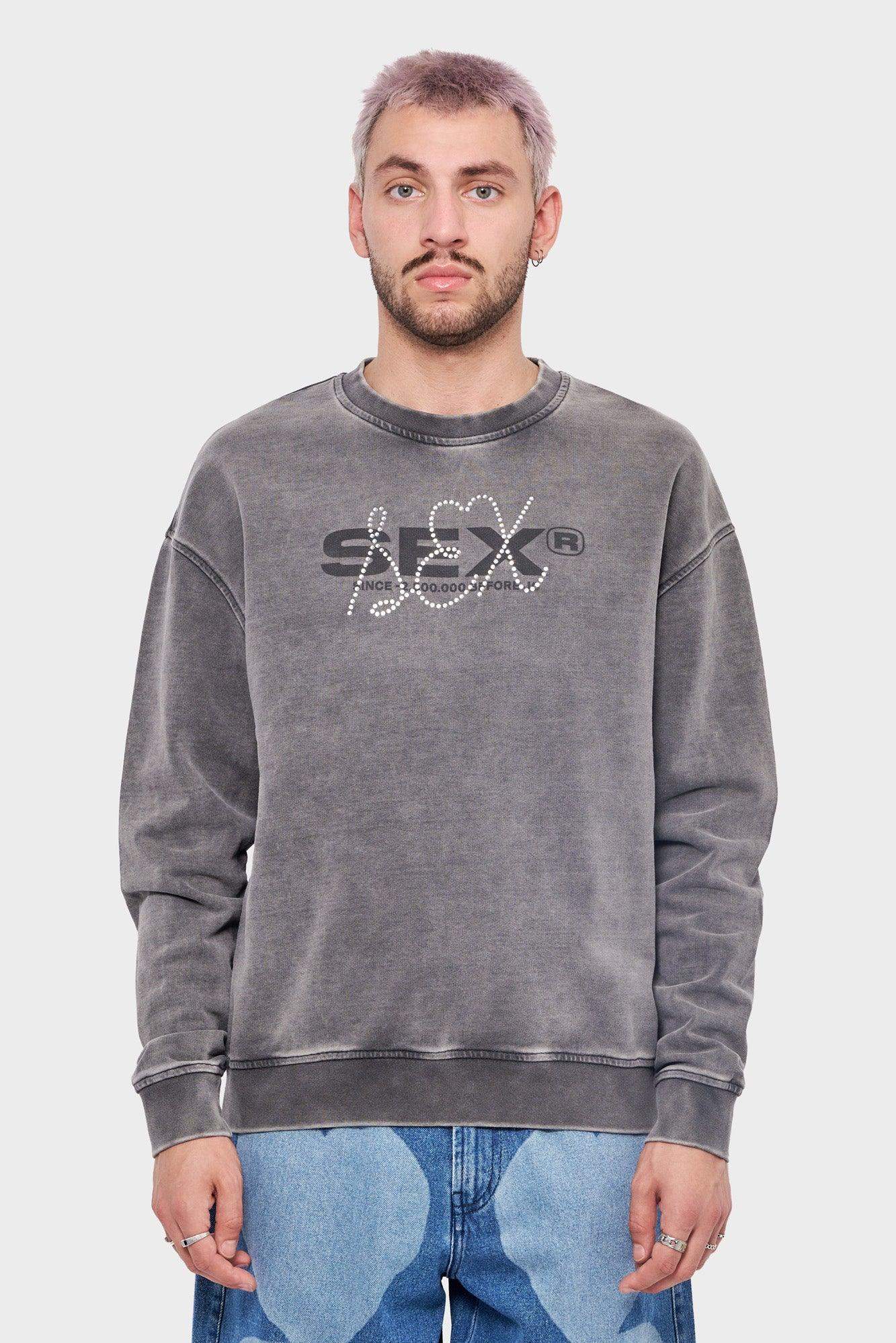 Mężczyzna w szarej bluzie z napisem SFX i dżetami, modne jeansy, styl streetwear