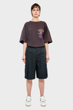 Kobieta w oversize'owej koszulce z nadrukiem i czarnych szortach cargo, sneakersy, styl streetwear