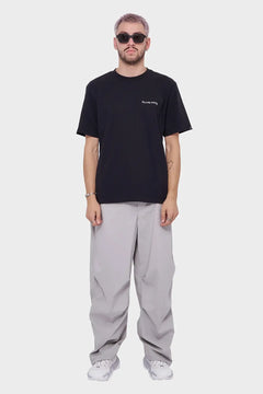 Mężczyzna w czarnym t-shircie z napisem, szarych szerokich spodniach i białych sneakersach