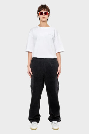 Osoba w białym t-shircie, czarnych spodniach dresowych, białych sneakersach i okularach przeciwsłonecznych, styl streetwear.