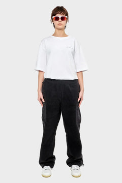 Osoba w białym t-shircie, czarnych spodniach dresowych, białych sneakersach i okularach przeciwsłonecznych, styl streetwear.