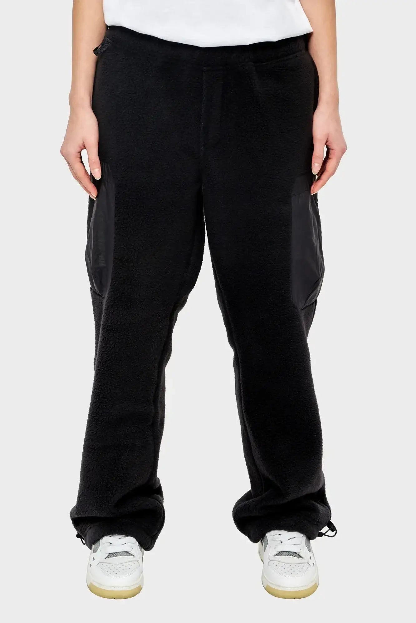 Czarne polarowe spodnie unisex z kieszeniami cargo, styl streetwear, białe sneakersy
